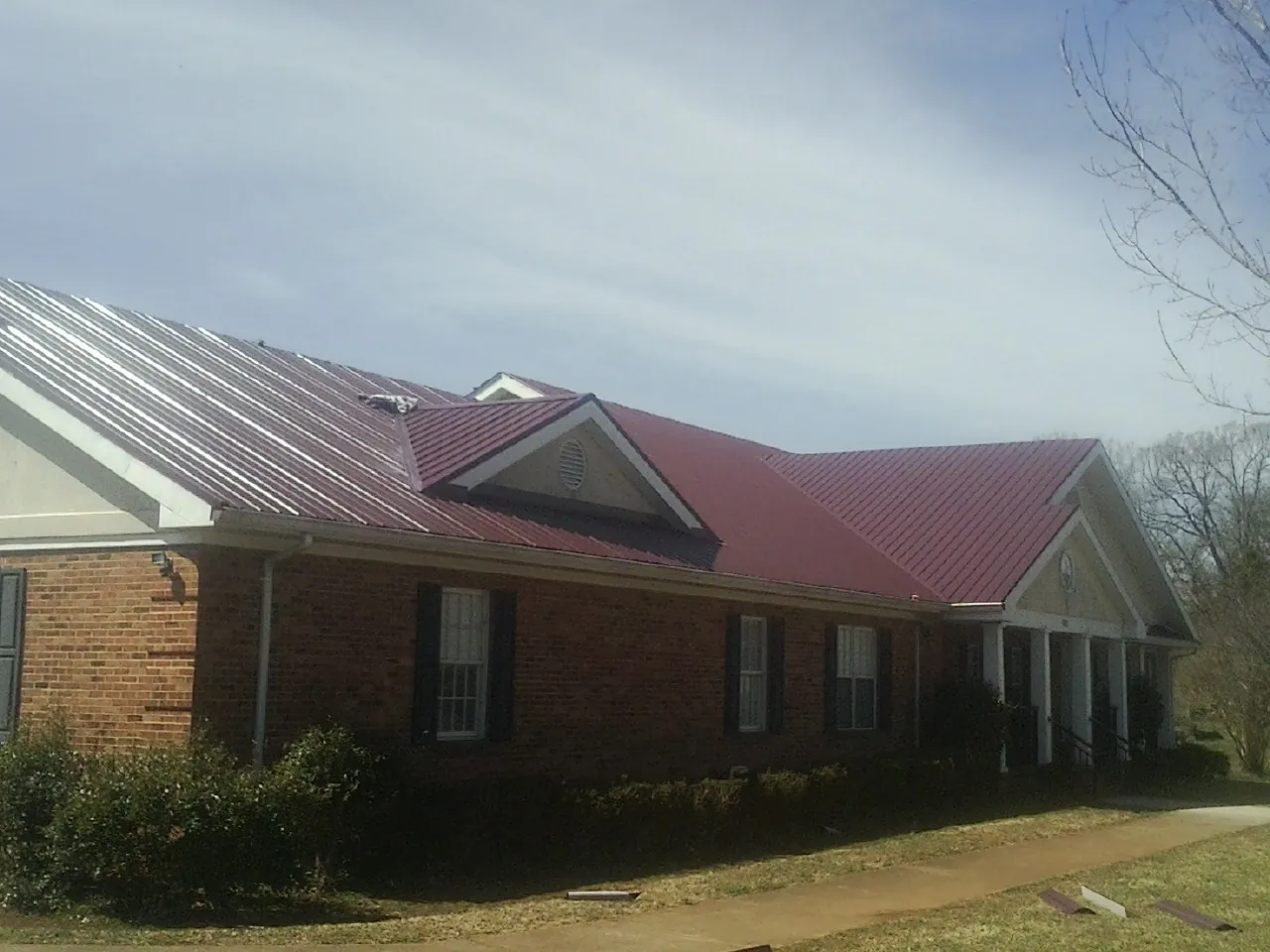 Red metal roof with gabled entries on a long brick building, from a Hail Damage Roof Repair job in Hattiesburg