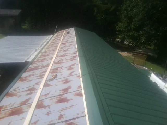 Old rusted panels beside newly installed green metal roofing — Wind Damage Roof Repair by Roofing Brothers in Hattiesburg