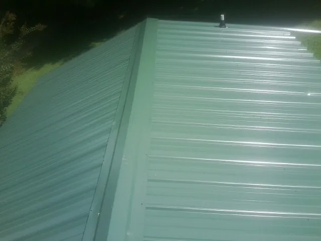 New green metal panels meeting at the ridge of a roof — Flat Roof Repair work by our crew in Hattiesburg