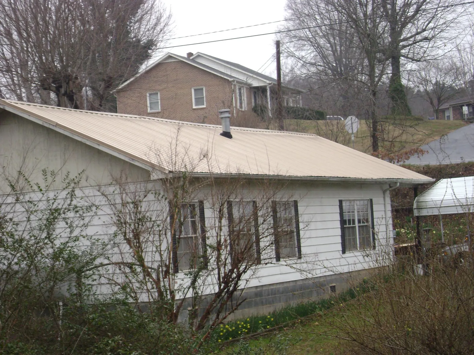Tan metal roof on a white sided house set into a hillside — Commercial Roofing by Roofing Brothers in Hattiesburg