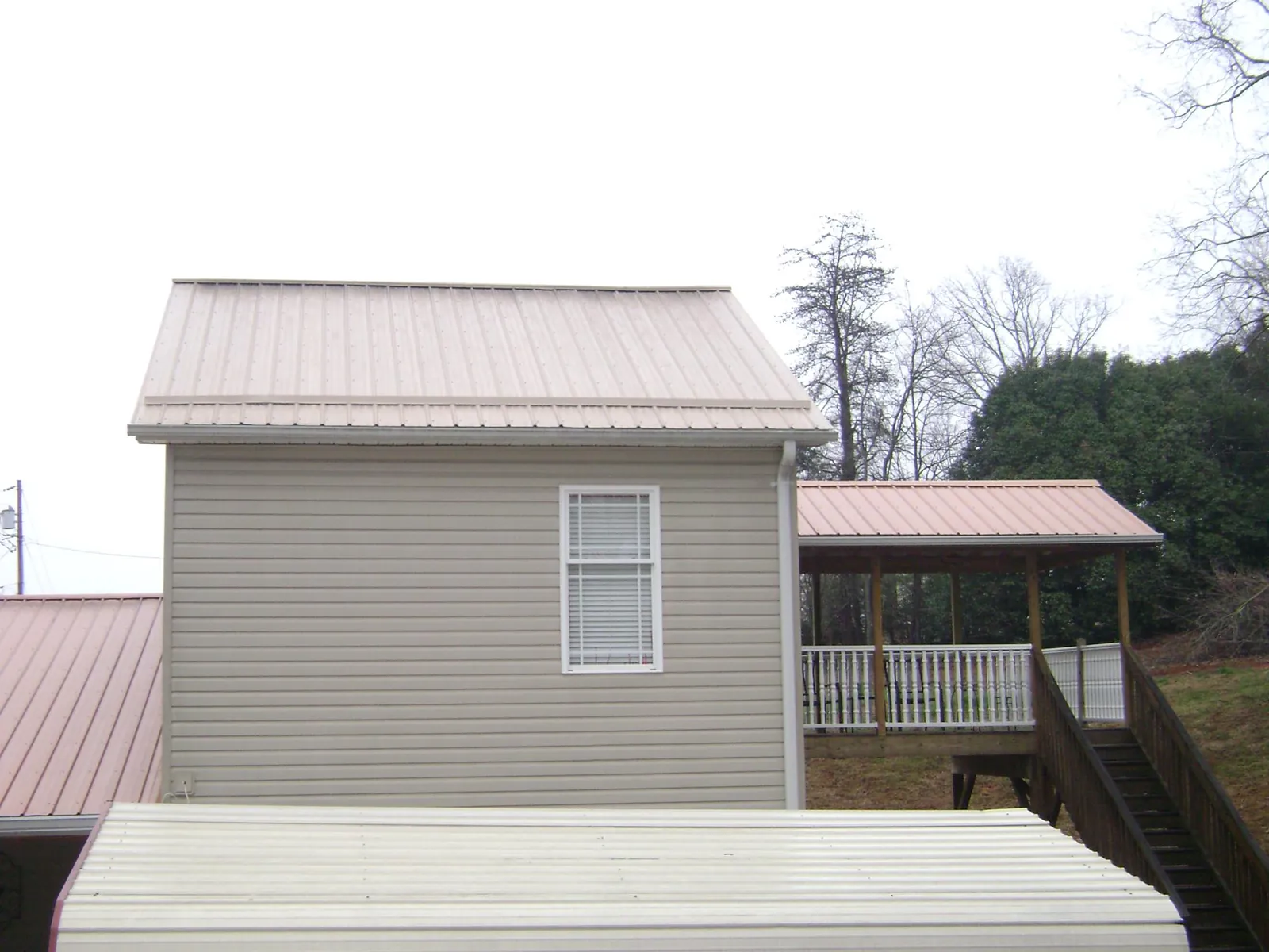 Tan metal roofs on a two story addition and attached porch, from a Roof Replacement job in Hattiesburg